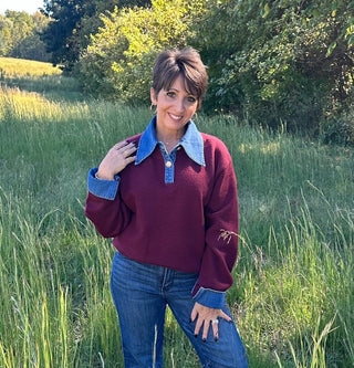 Woman wearing a maroon sweater with blue collar and cuffs in a grassy field